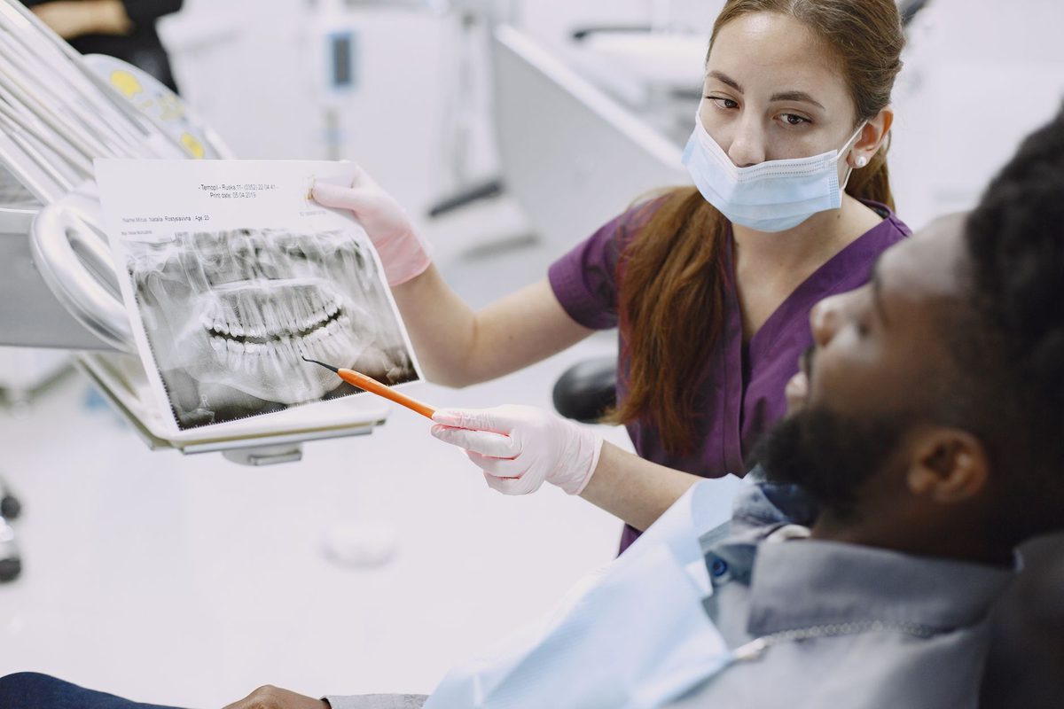 A dental assistant showing a patient his X-ray and pointing to a tooth