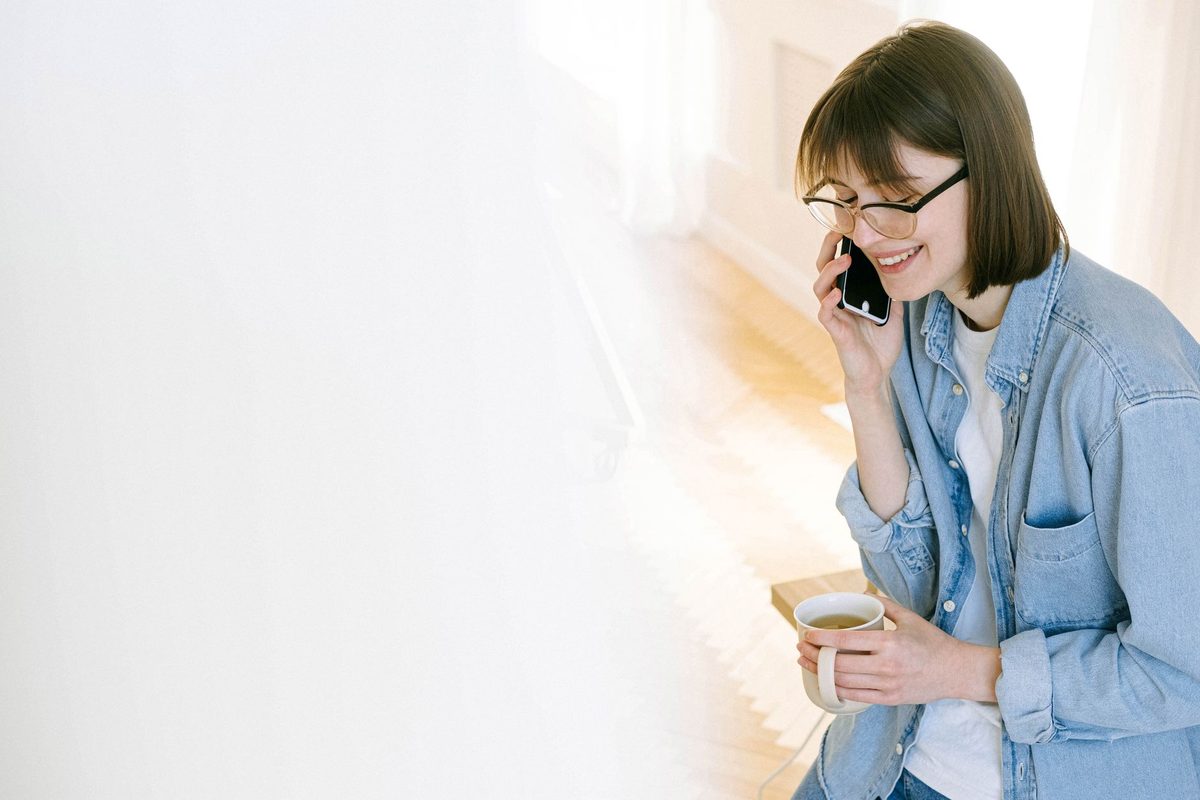 A woman at home making a phone call with a cup of coffee in her hand