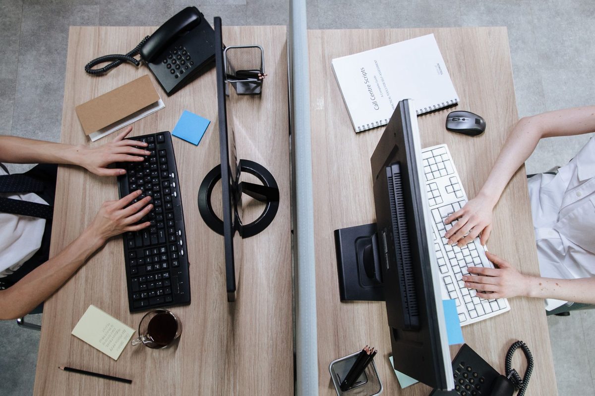 An overhead view of two desks with keyboards, monitors and desk phones