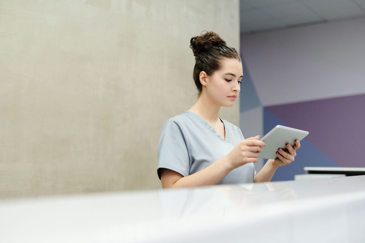 A receptionist in scrubs checking an appointment on a tablet at the front desk